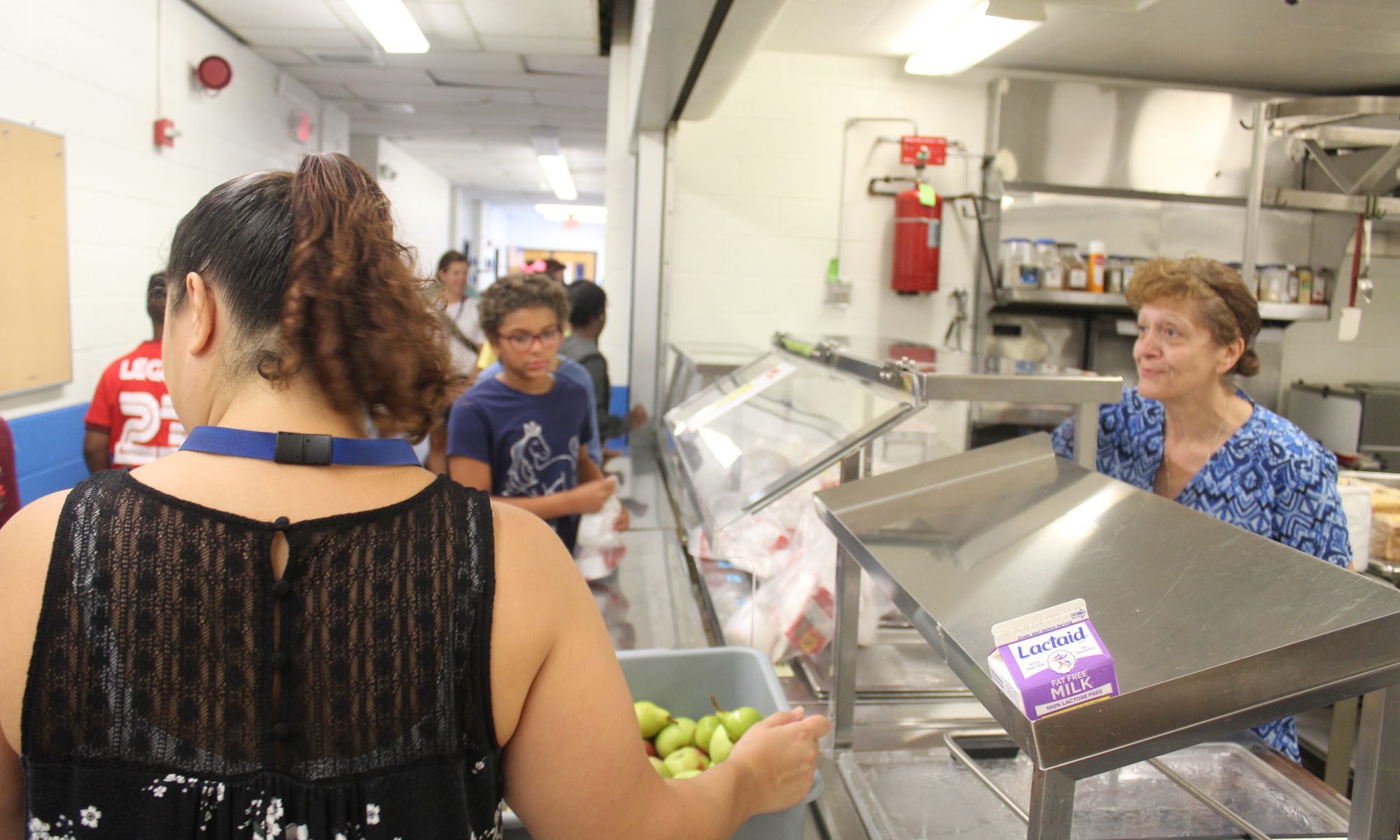 A cafeteria server smiles as middle school students go down the line for food.