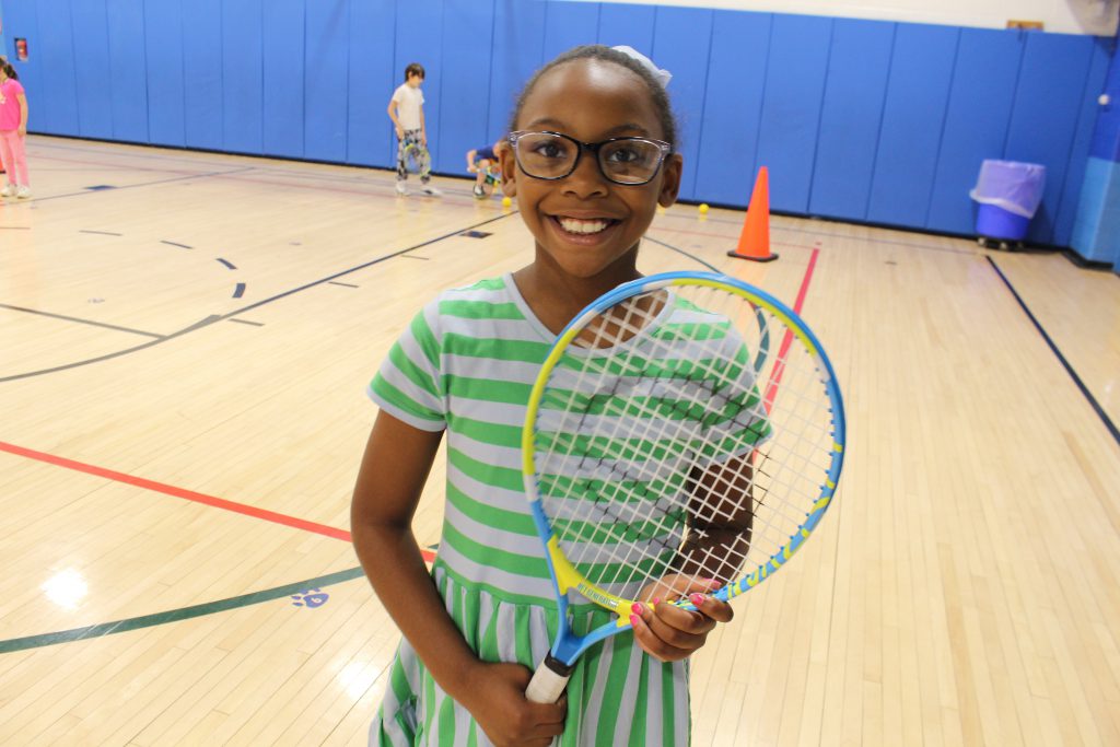 a girl is holding a racquet and smiling. 