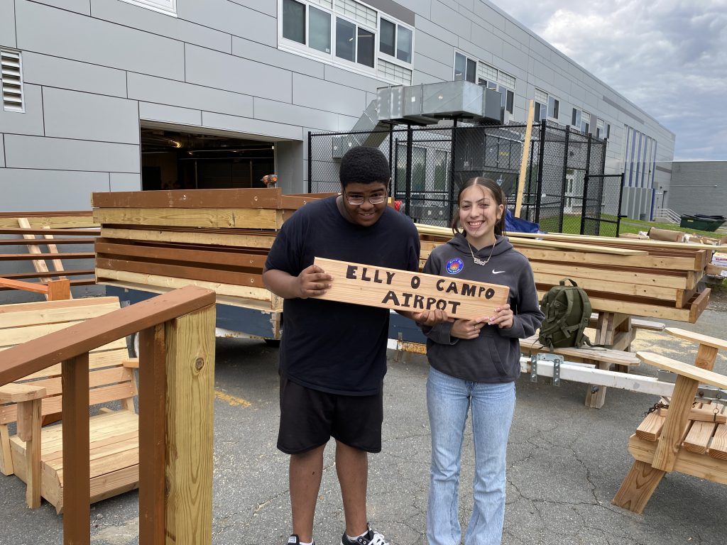 two students are posing and holding a wood sign that says Elly O Campo Airport 