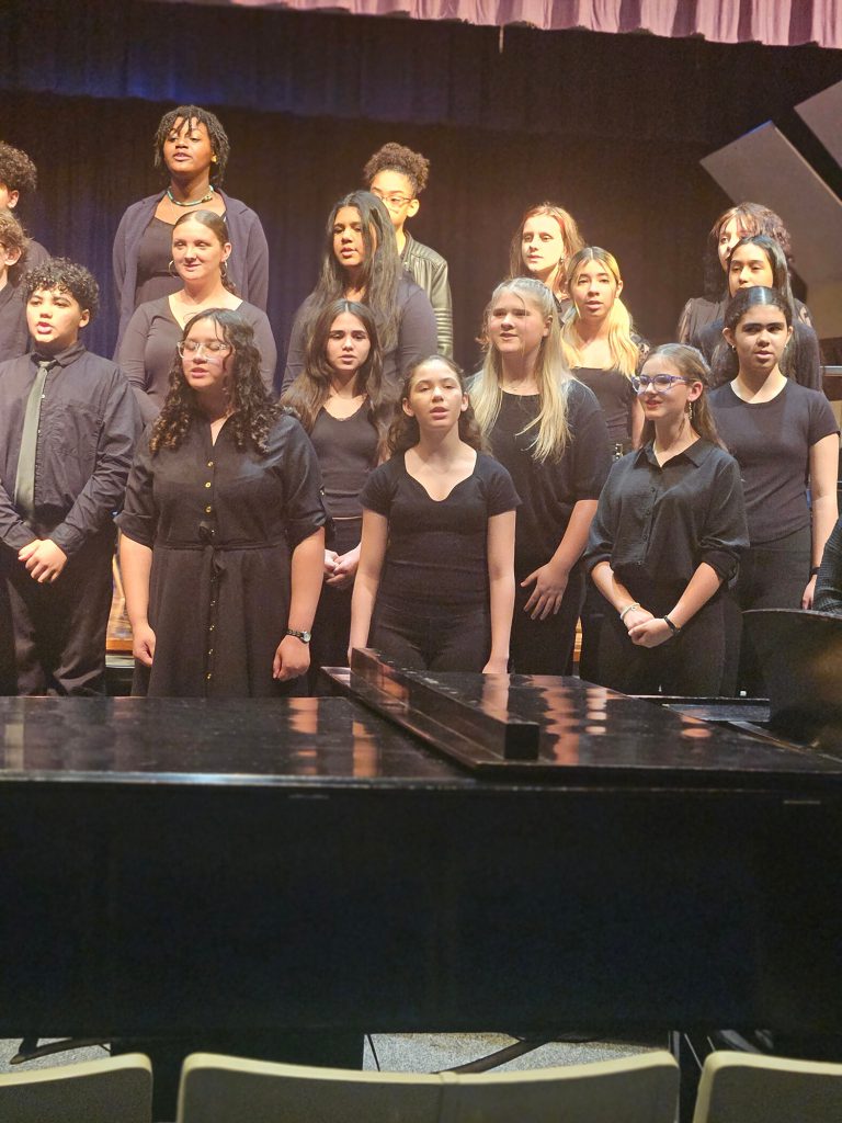 Group of students dressed in black on stage singing.