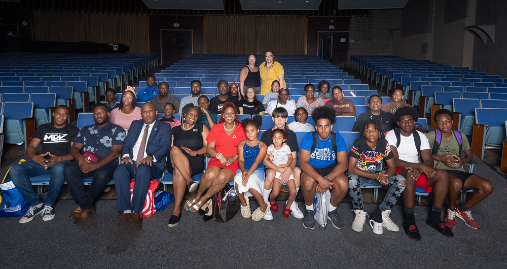 a group of students, teachers and community participants are seated in the auditorium. 