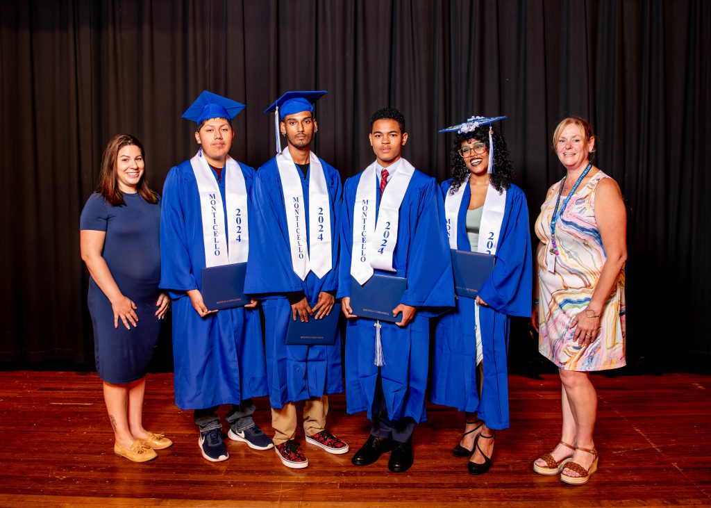 four students in caps and gowns are posing on stage with two assistant principals 