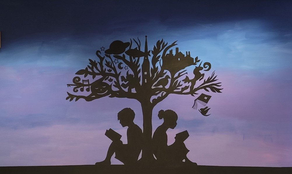 photo of a mural. The mural depicts the silhouette of two children reading under a tree