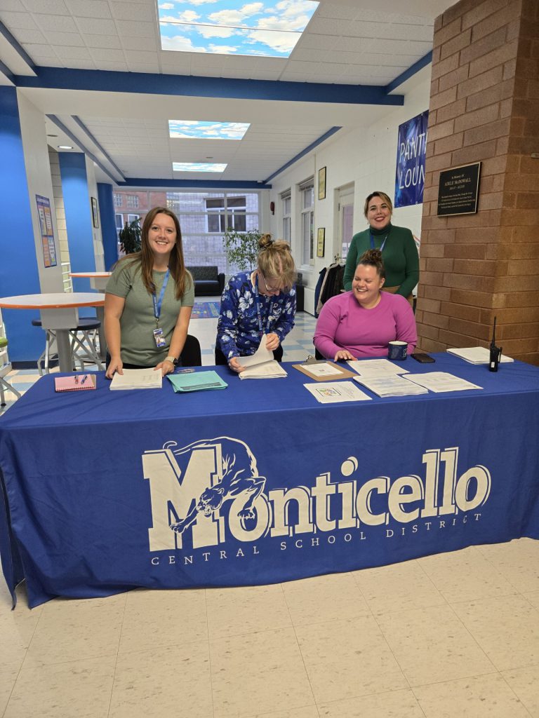 Ms. Jayme Abrams, School Psychologist, Ms. Sharon Zimmerman, Social Worker, Miss Samantha Acito, Principal’s Secretary, and Kelly Gallagher, Social Worker.  (left to right and all RJK Staff) are posing behind a table. 