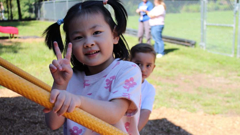 a young girl gives a "peace" sign with her hands on the playground