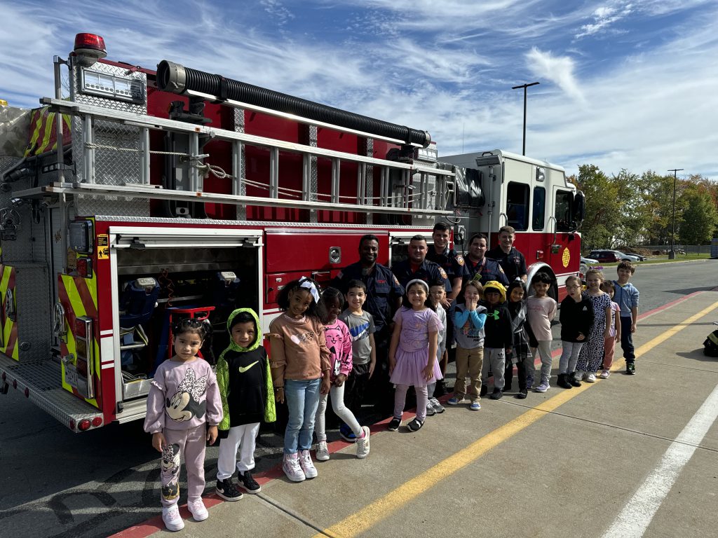 a group of firefighters are posing in front of a firetruck with a class of young students 