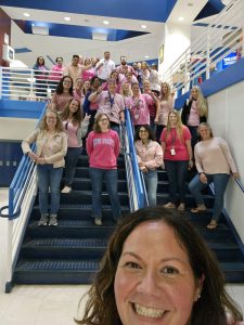 a group of teachers wearing pink shirts and denim jeans are posing on the stairs