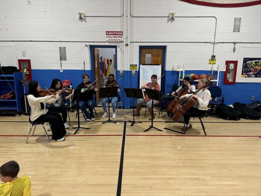 the high school string performers are performing in front of a group of children