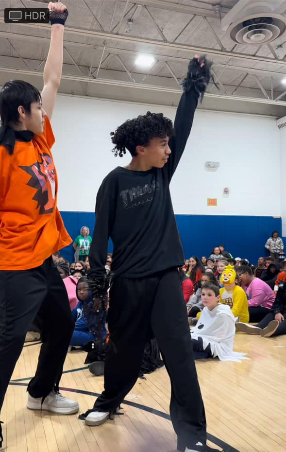 two dancers perform in front of a large group of elementary school children