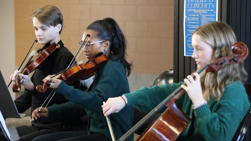 three students are playing violins