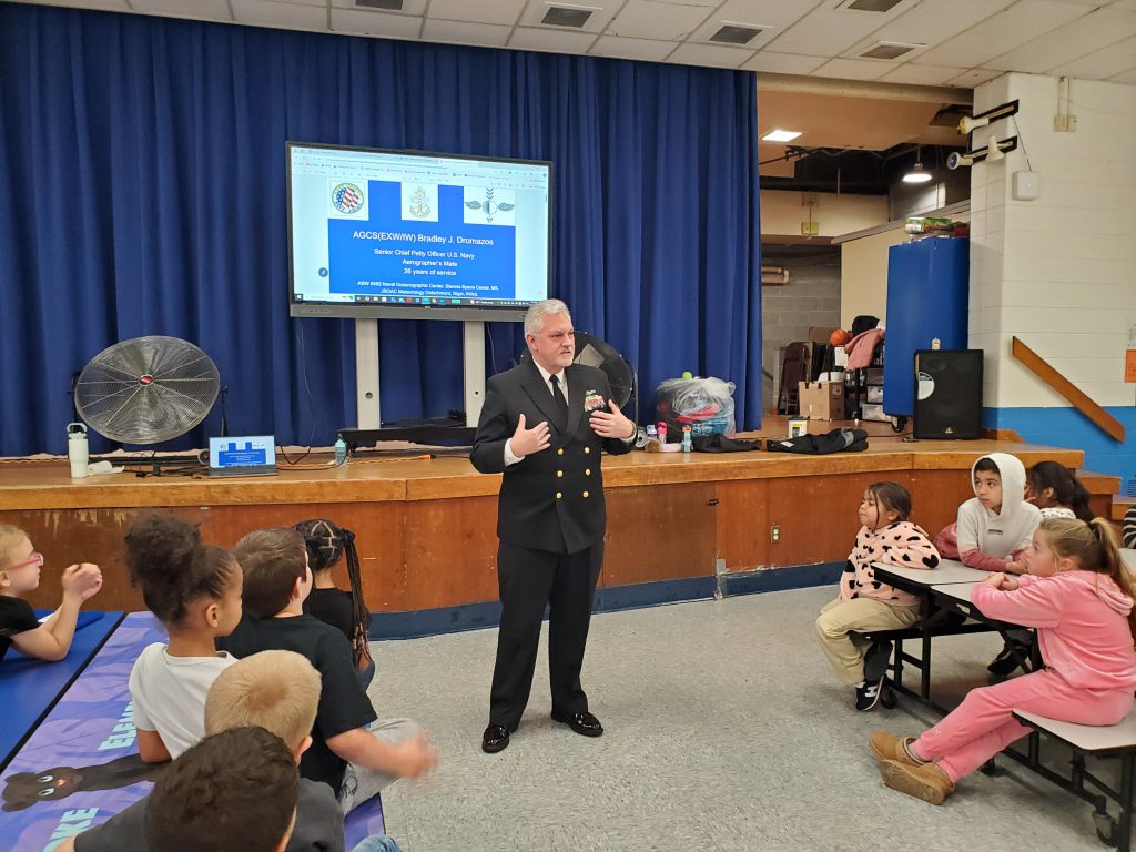 a veteran addresses a group of schoolchildren seated in the cafeteria