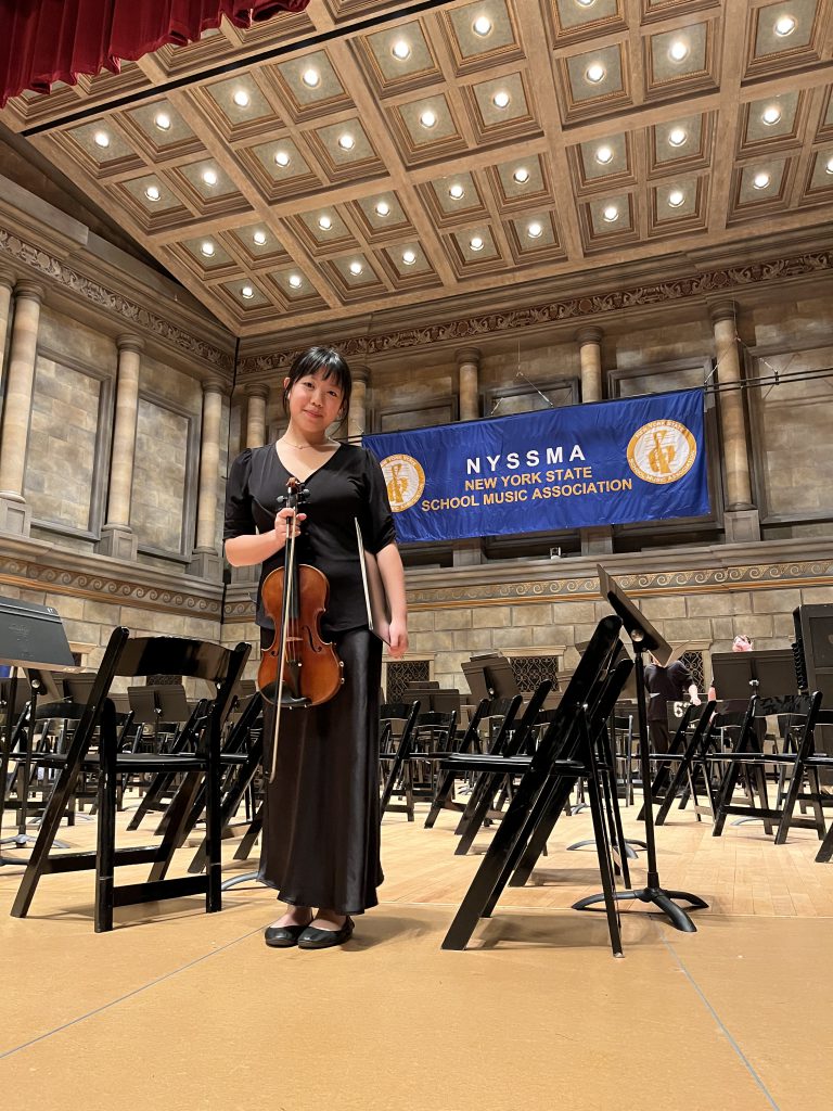 Belle is posing on stage holding a violin