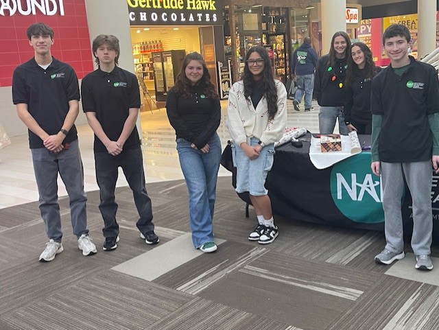 students from the academy of finance are posing near the table where they were providing gift wrap services at the mall. 