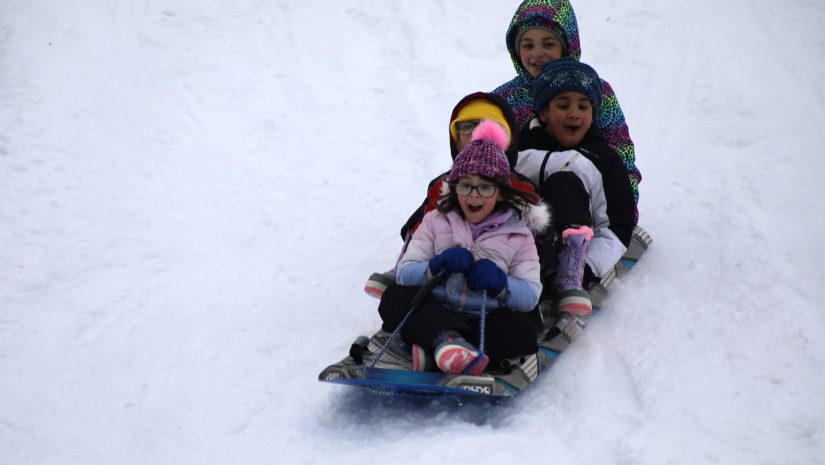 four students are on a sled sliding down the hill. They are all smiling.