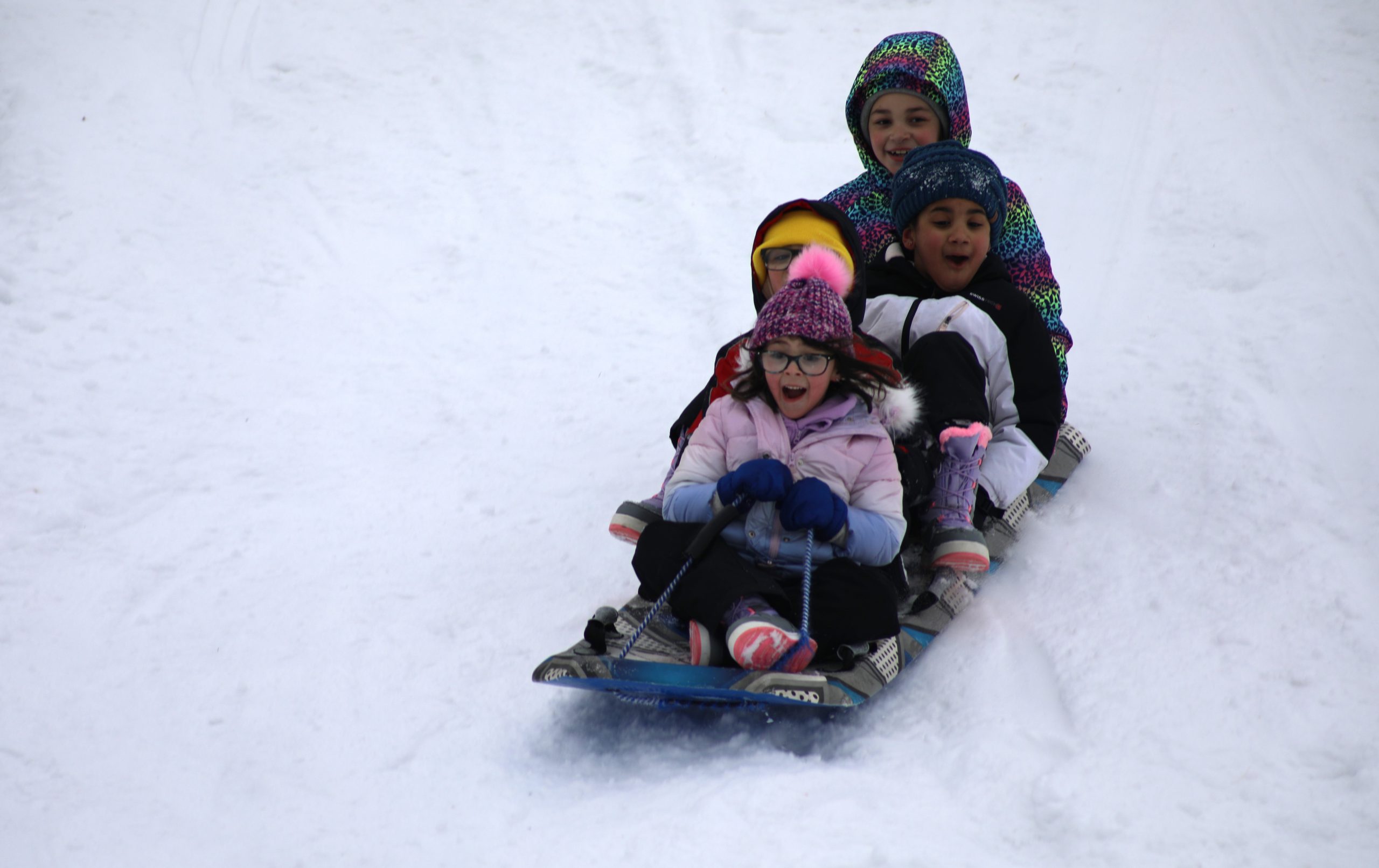 four students are on a sled sliding down the hill. They are all smiling.