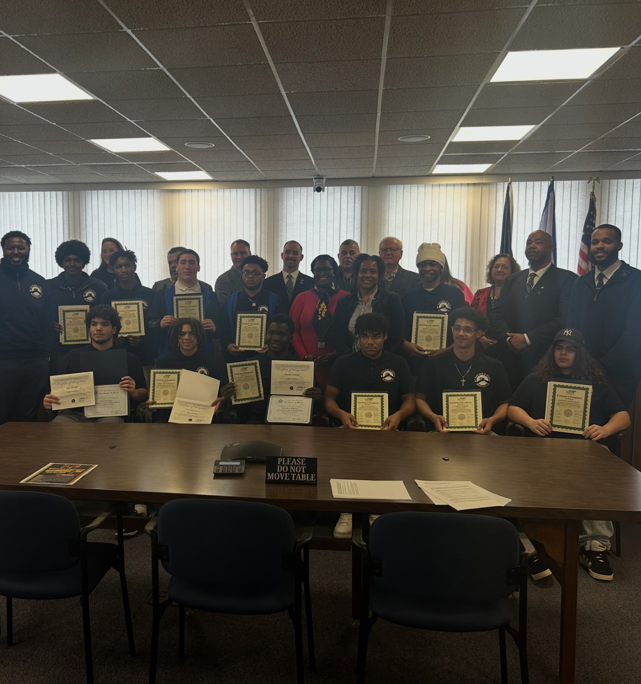 a group of students are seated around a table with legislators. The students are holding up certificates they received during the event. 