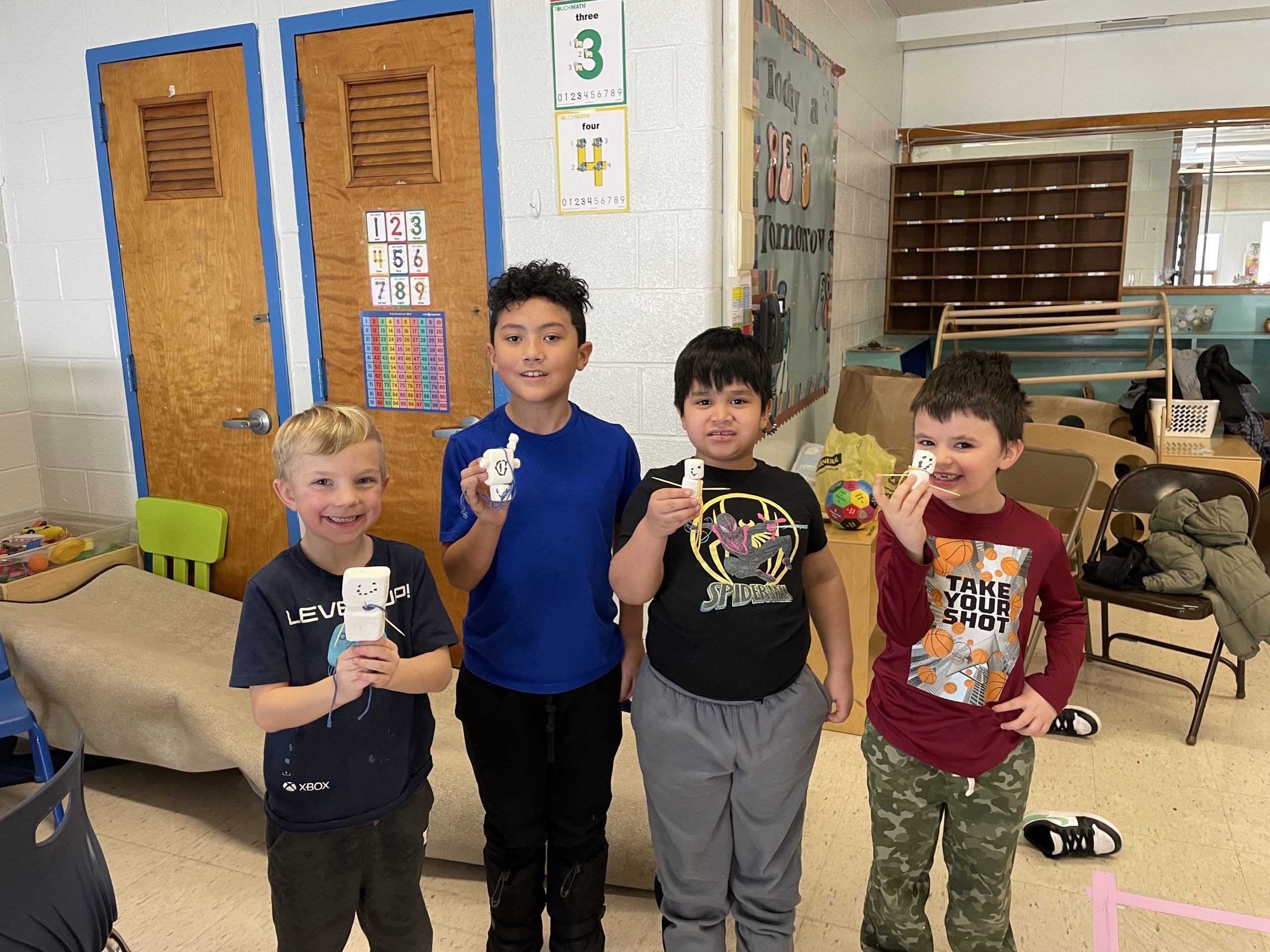 four students are holding up marshmallow snow men that they created as part of the indoor activities on winter fun day. 