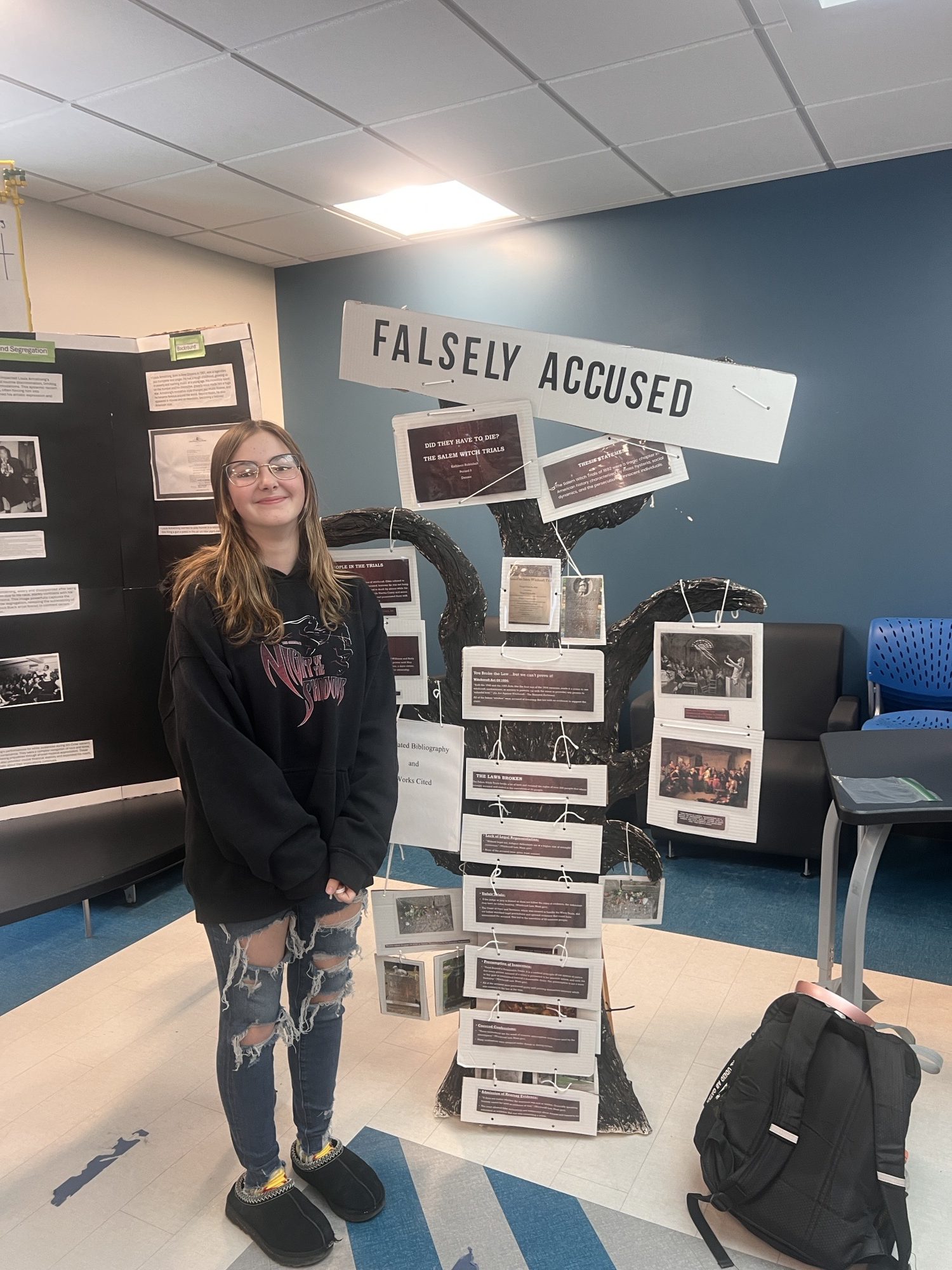 a student poses next to a display of her research project during the local National History Day competition. 