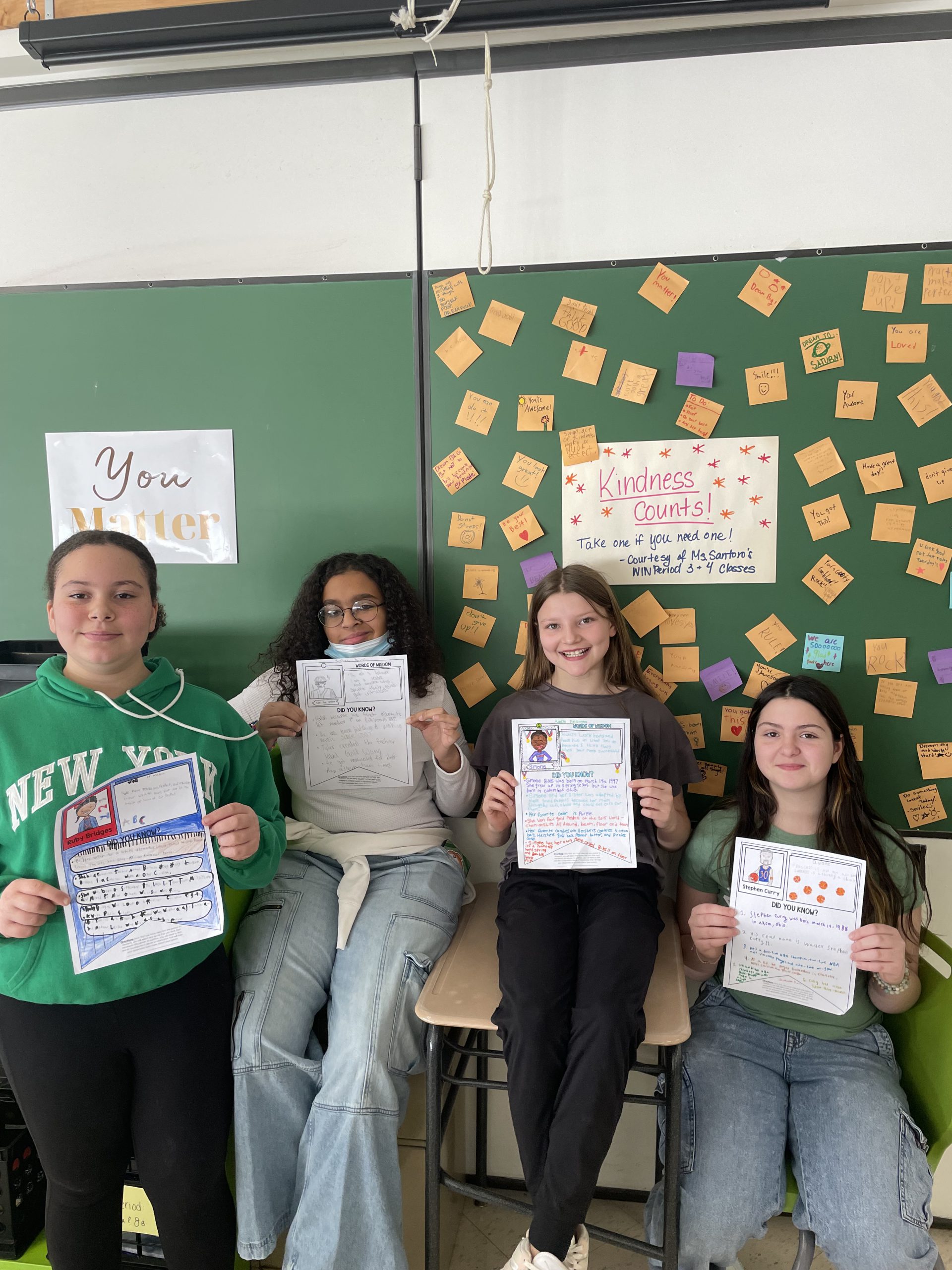 four students smile for the camera and hold up the projects they've been working on. 