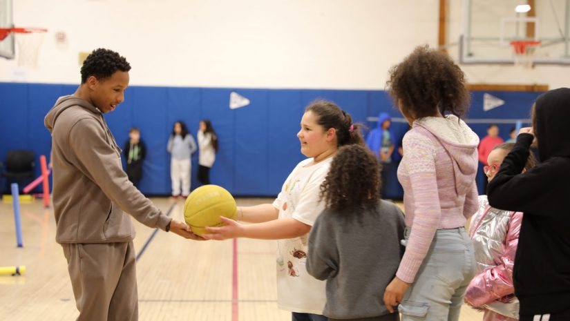 a high school student is handing a basketball to a younger student