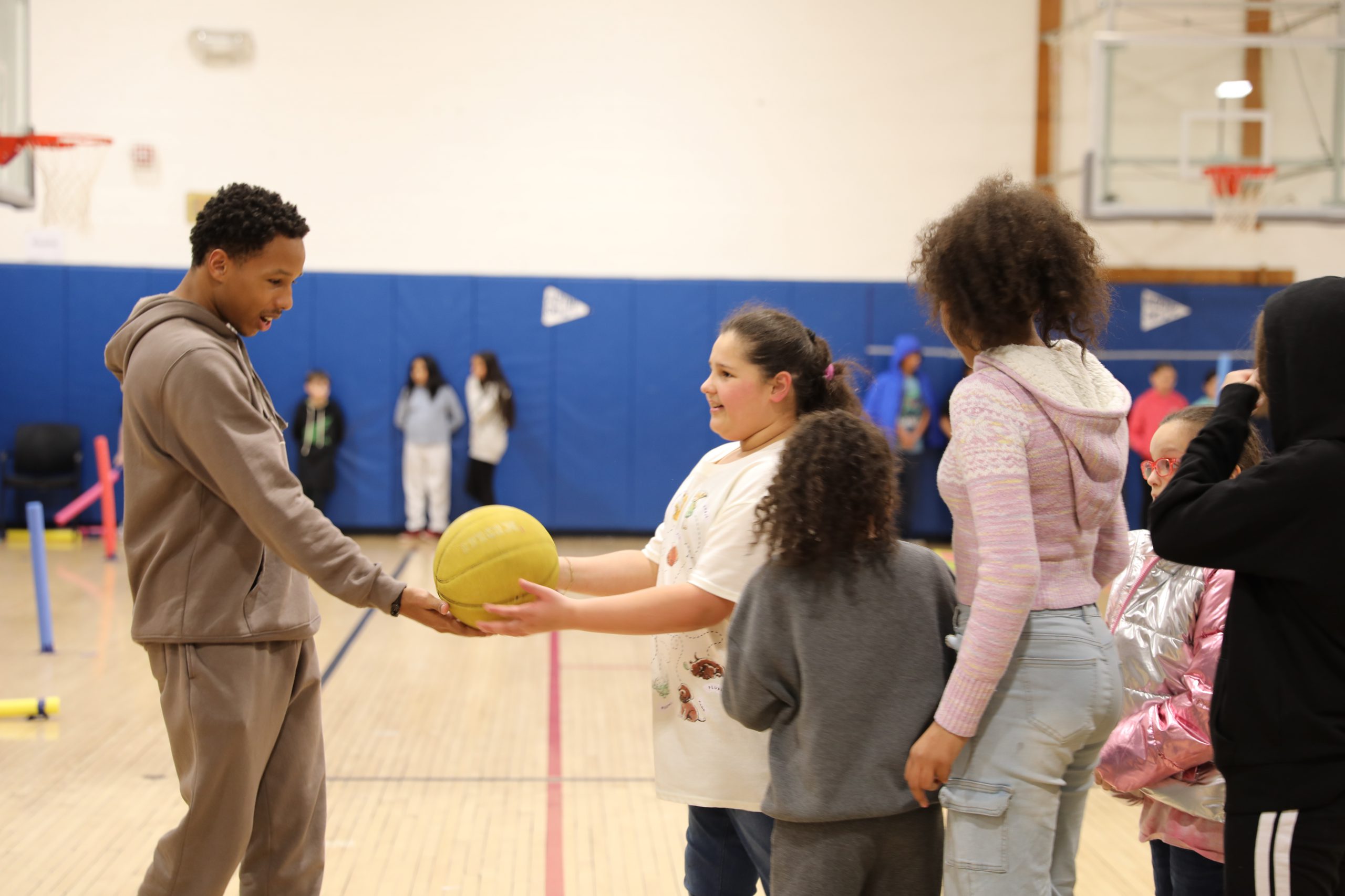 a high school student is handing a basketball to a younger student