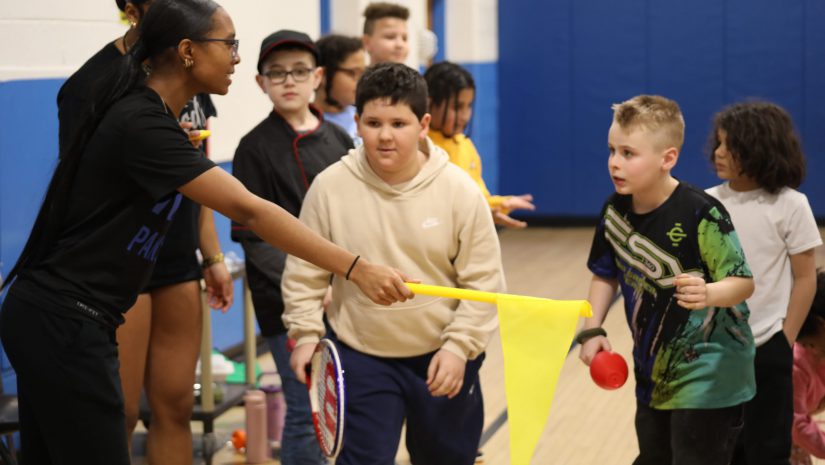 two students are lined up to begin a race. An older student is holding a flag, about to start the race