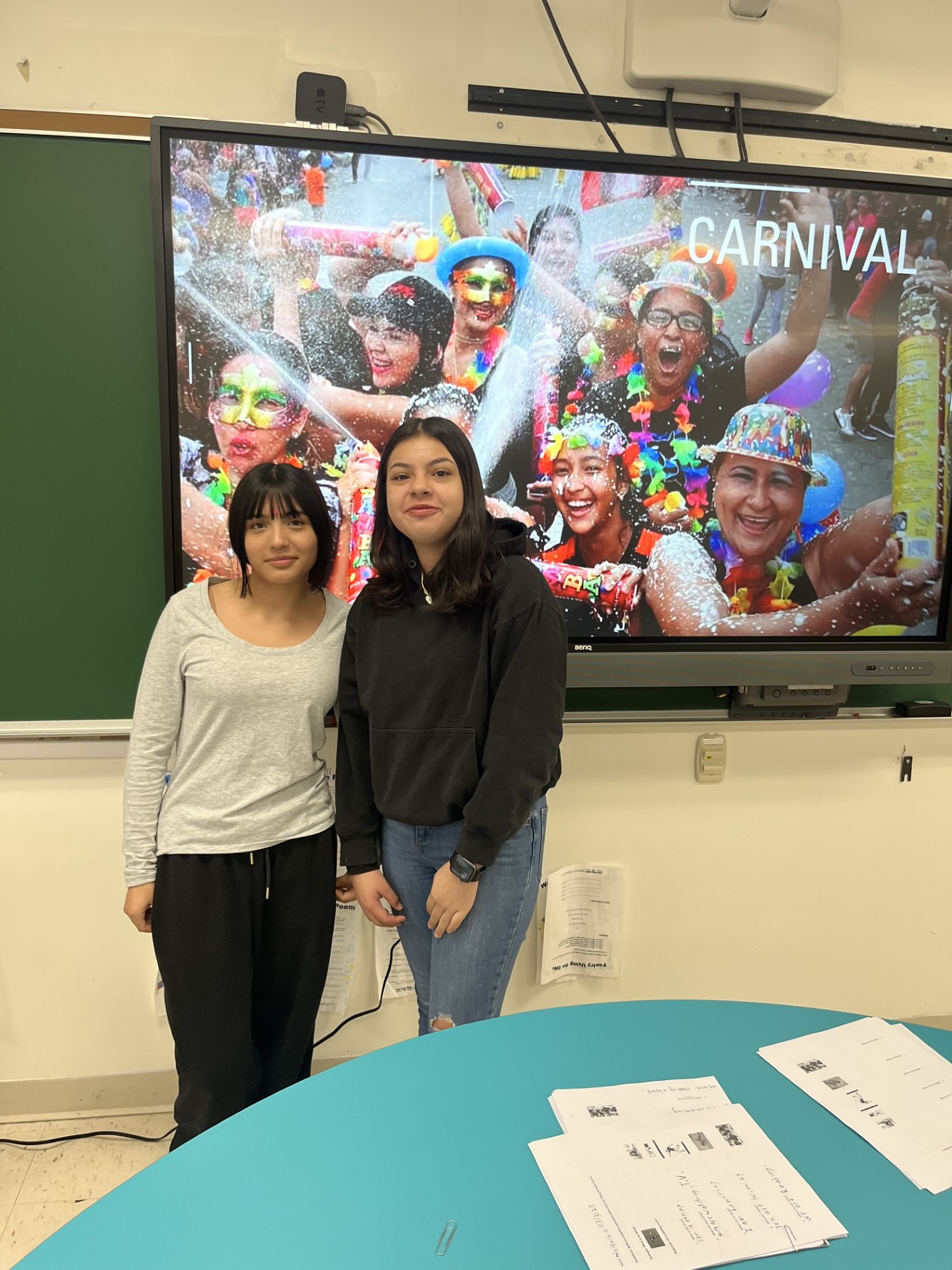 two students pose behind a slide show of carnival